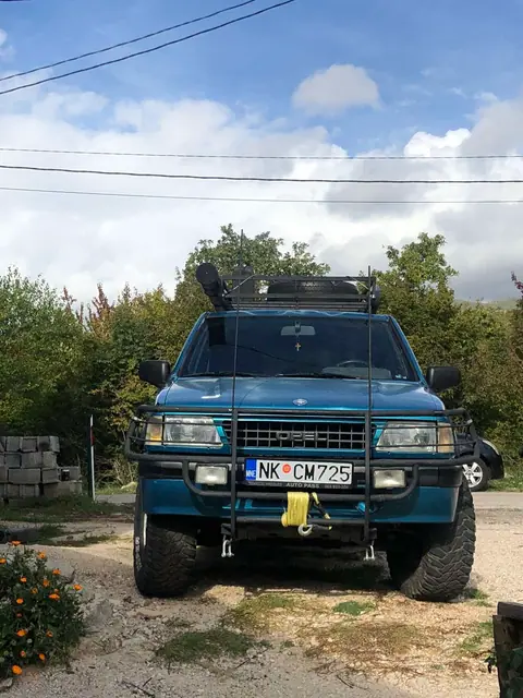 Plavi terenac fotografisan sprijeda na makadamskoj podlozi
