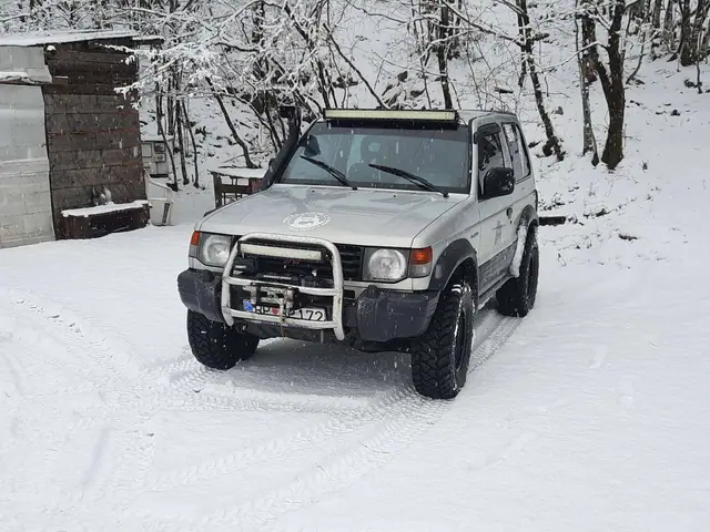Srebrni terenac parkiran pored snježne šume