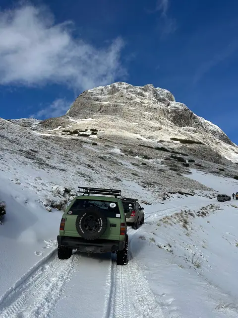 Zeleni terenac na snježnom putu ispod planinskog vrha